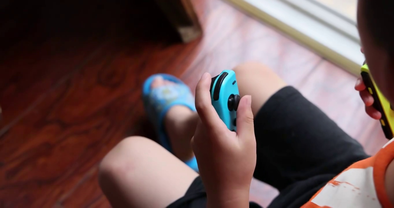 暑假生活：小男孩使用无线手柄控制掌机玩耍视频素材