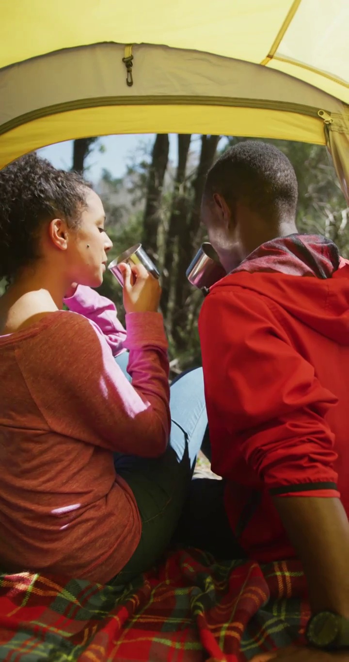 垂直视频微笑的非洲裔美国夫妇徒步旅行，喝咖啡坐在帐篷视频下载