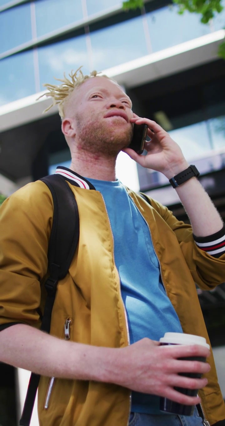 一个留着脏辫的白化病男子用智能手机站在城市街道上的垂直视频视频下载