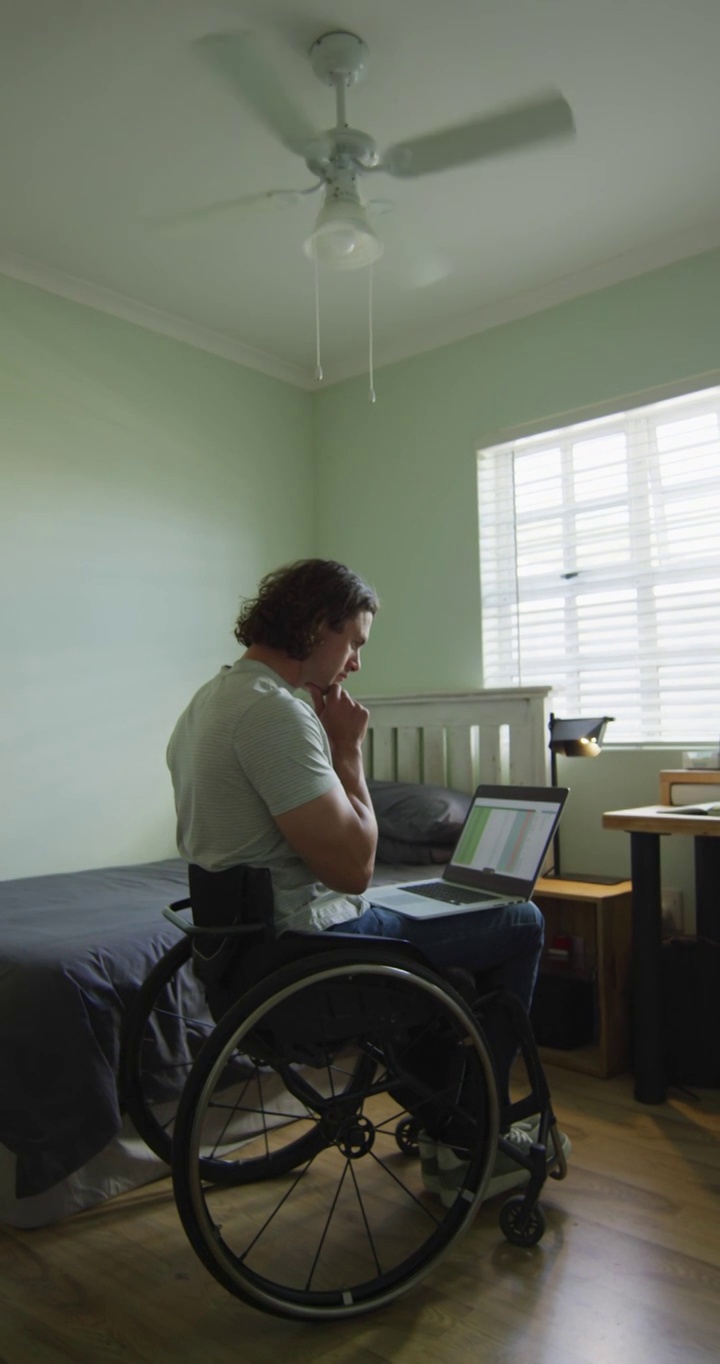 白人残疾人坐在轮椅上使用笔记本电脑的垂直视频视频下载