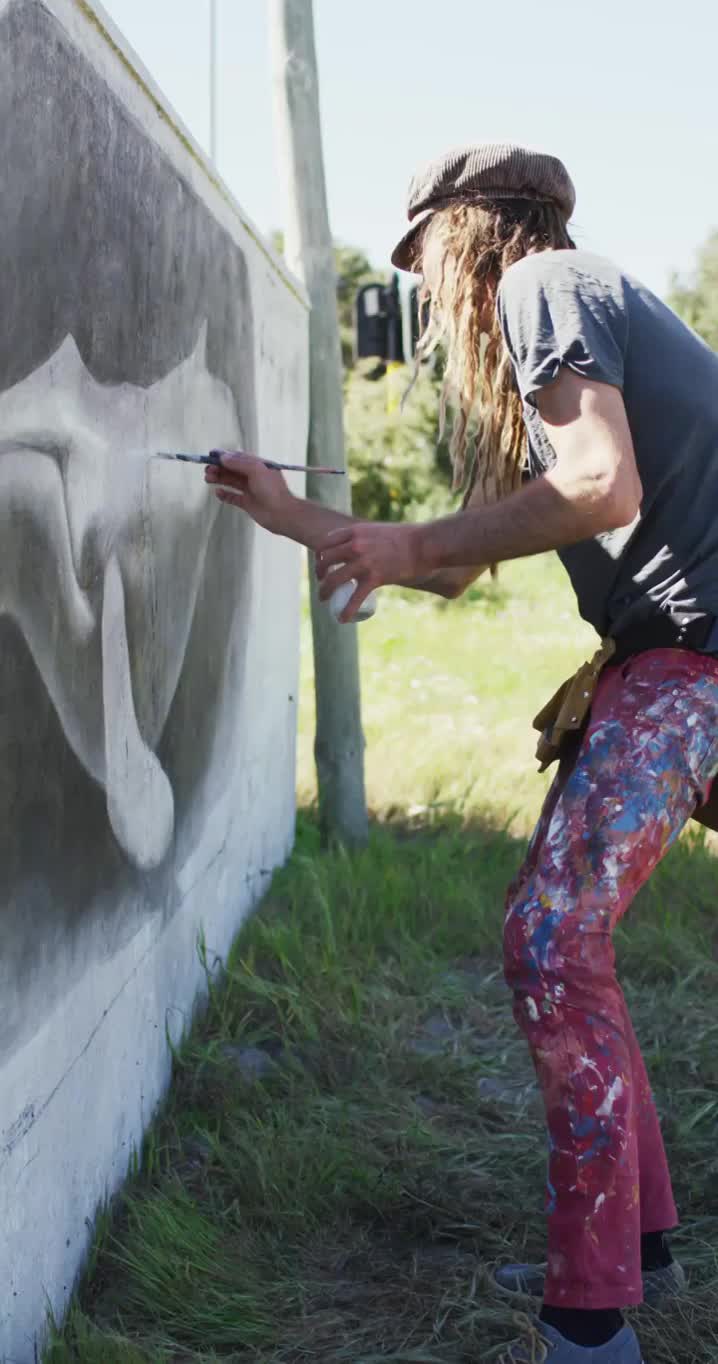 白人潮男艺术家长头发在墙上画鲸鱼壁画的垂直视频视频下载