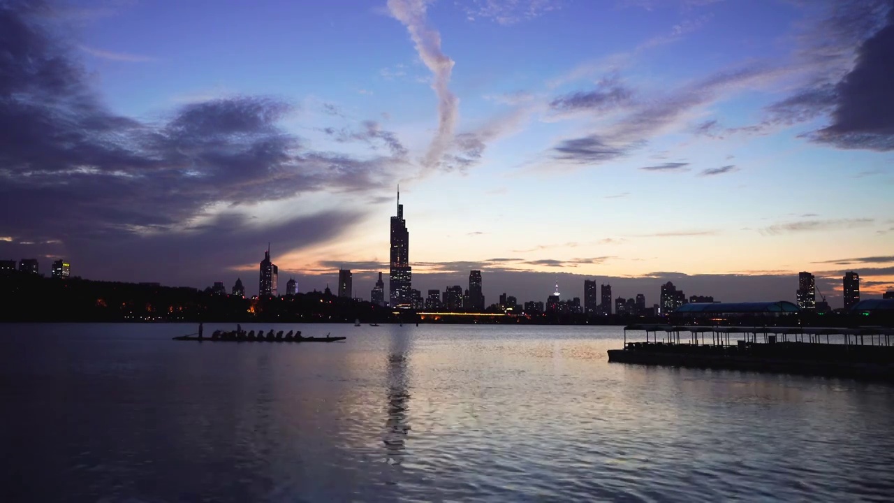 黄昏傍晚时分南京玄武湖上的龙舟训练和城市夜景风光视频下载