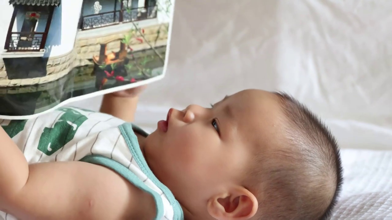 卧室床上婴儿双手拿着画册认真注视看书面部表情特写视频下载