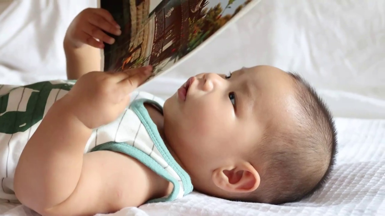 卧室床上婴儿双手拿着画册认真注视看书面部表情特写视频下载