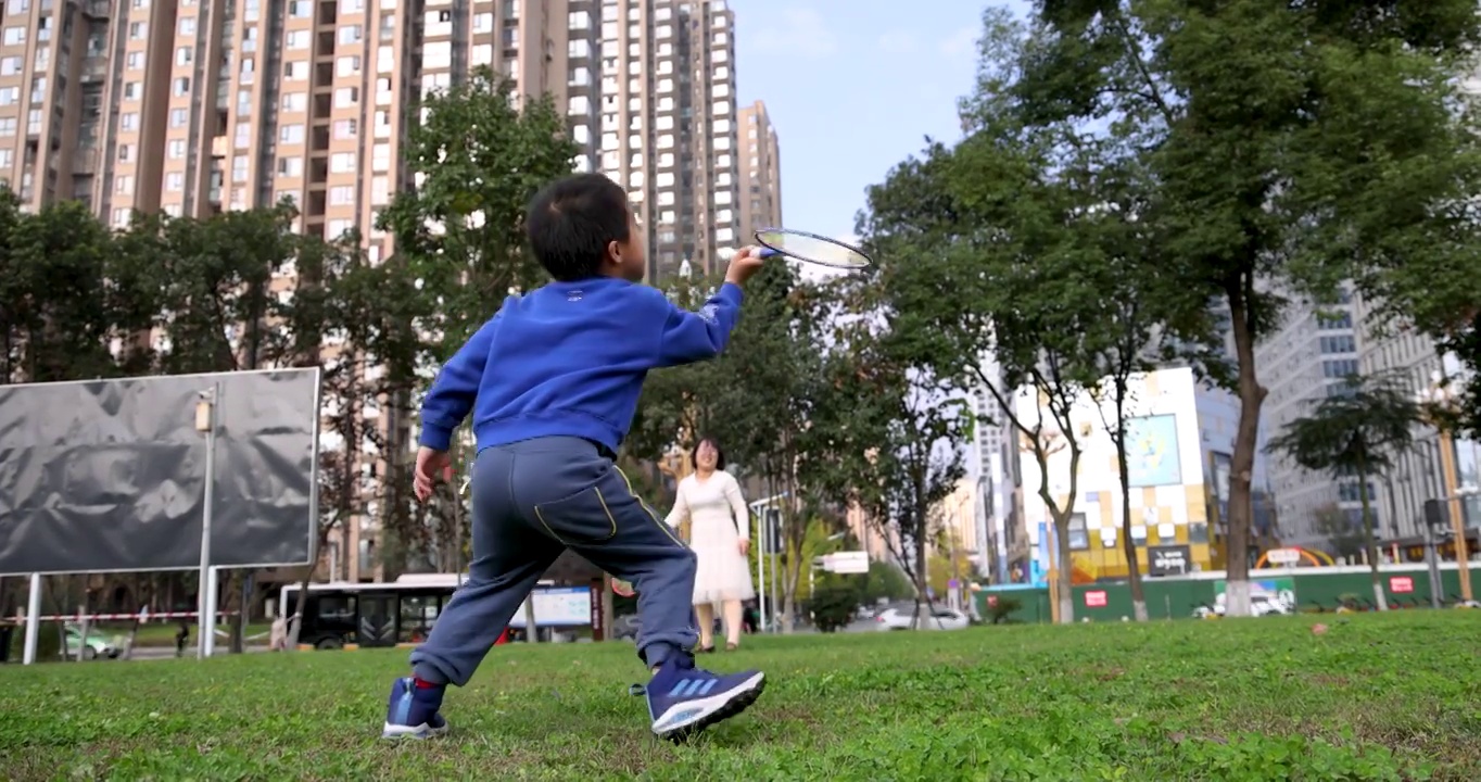 升格镜头下的体育运动：小男孩和母亲在城市草坪里打羽毛球视频下载