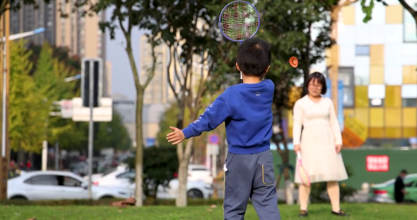 升格镜头下的体育运动：小男孩和母亲在城市草坪里打羽毛球视频下载