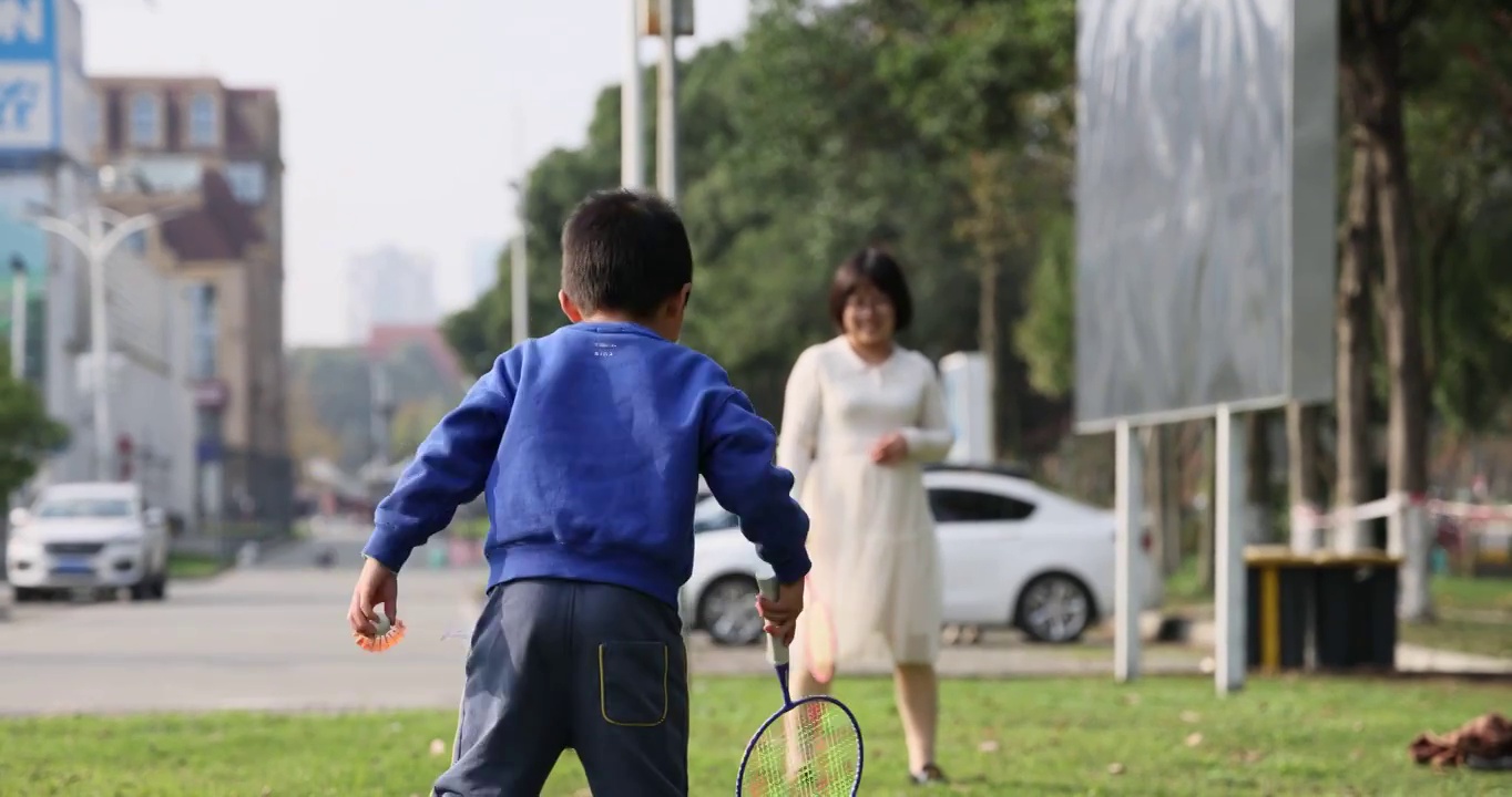 体育运动：母亲和儿子在城市草坪里打羽毛球视频下载