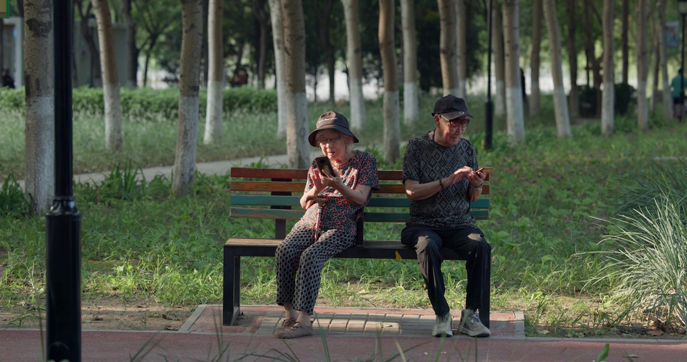 老年夫妇在公园长椅上各自看着自己的手机视频下载