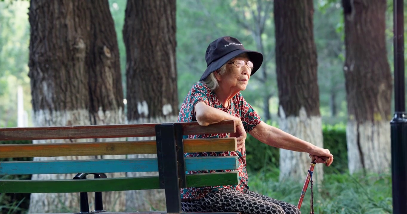 老年人手拄着拐棍孤独的坐在公园长椅上视频素材