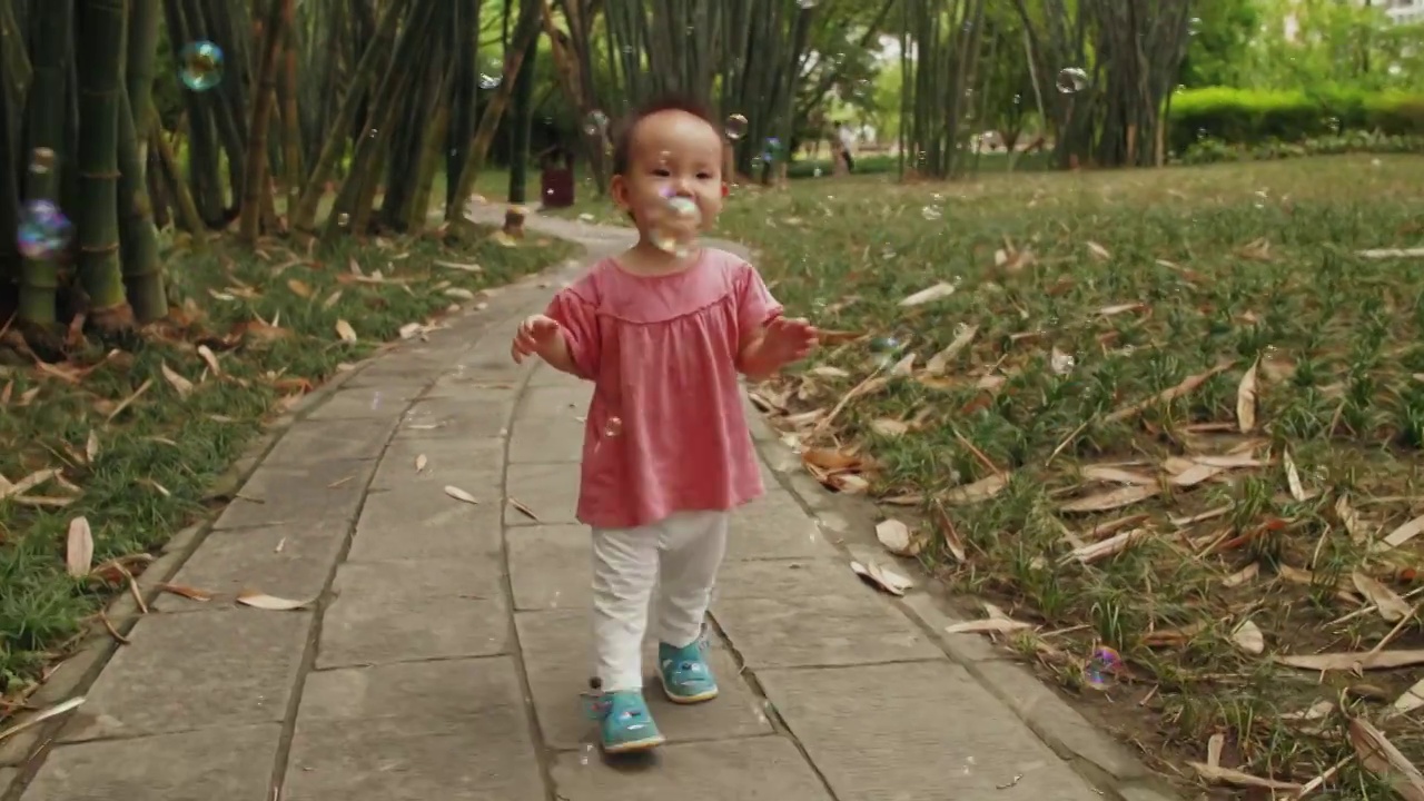 蹒跚学步的可爱小婴儿在公园里玩耍抓泡泡视频素材