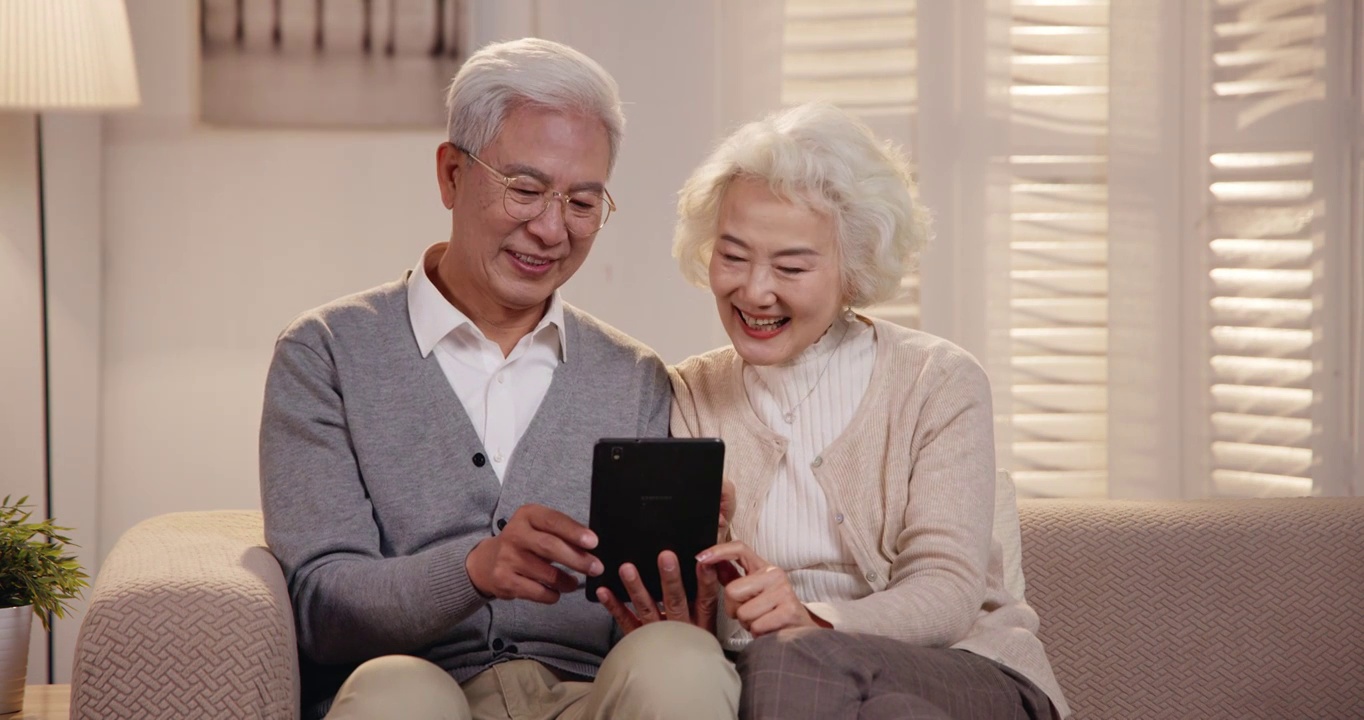 老年夫妇坐在沙发上看平板电脑视频下载