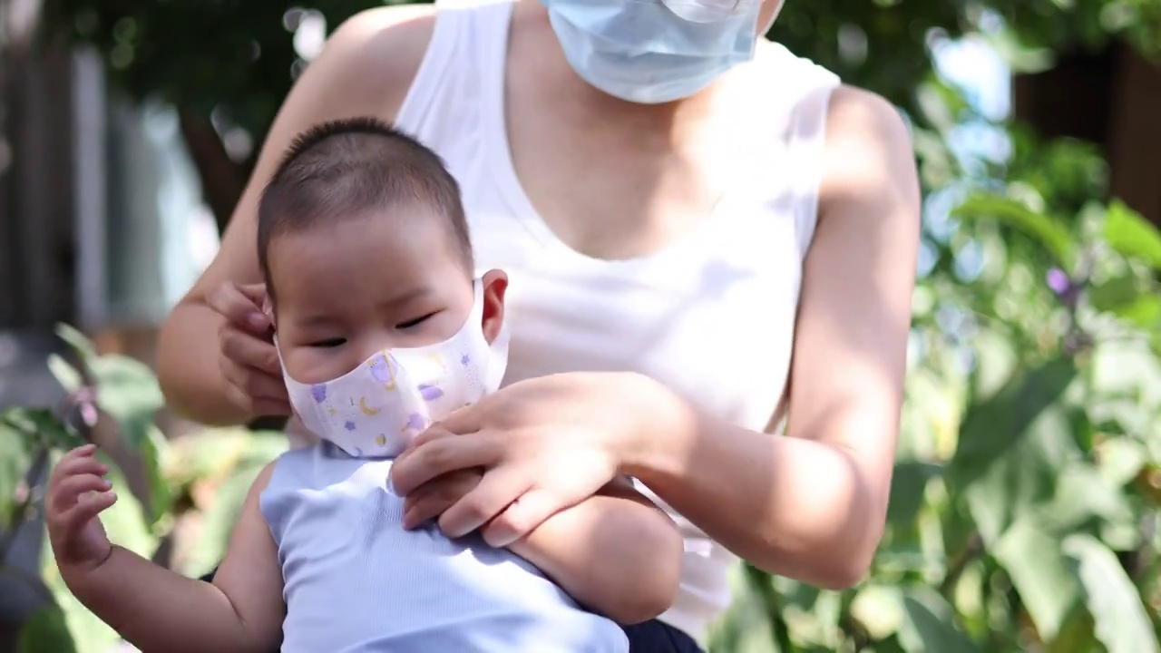 夏季户外树荫下妈妈给宝宝戴上口罩预防病毒流感视频下载