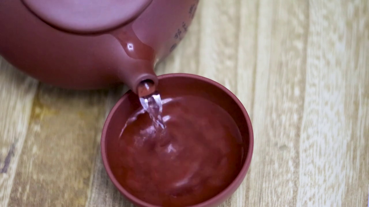 将茶壶中泡好的茶水倒入木制桌面上的紫砂茶杯中视频素材