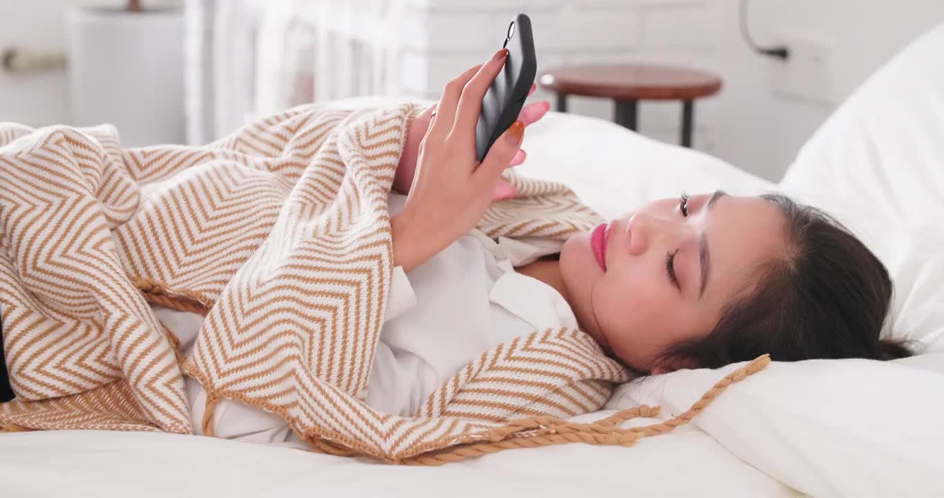 年轻女人趴在床上看手机美女网络视频下载