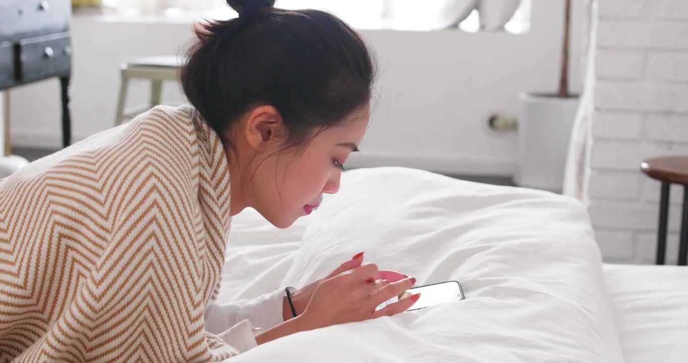 年轻女人趴在床上看手机美女网络视频素材