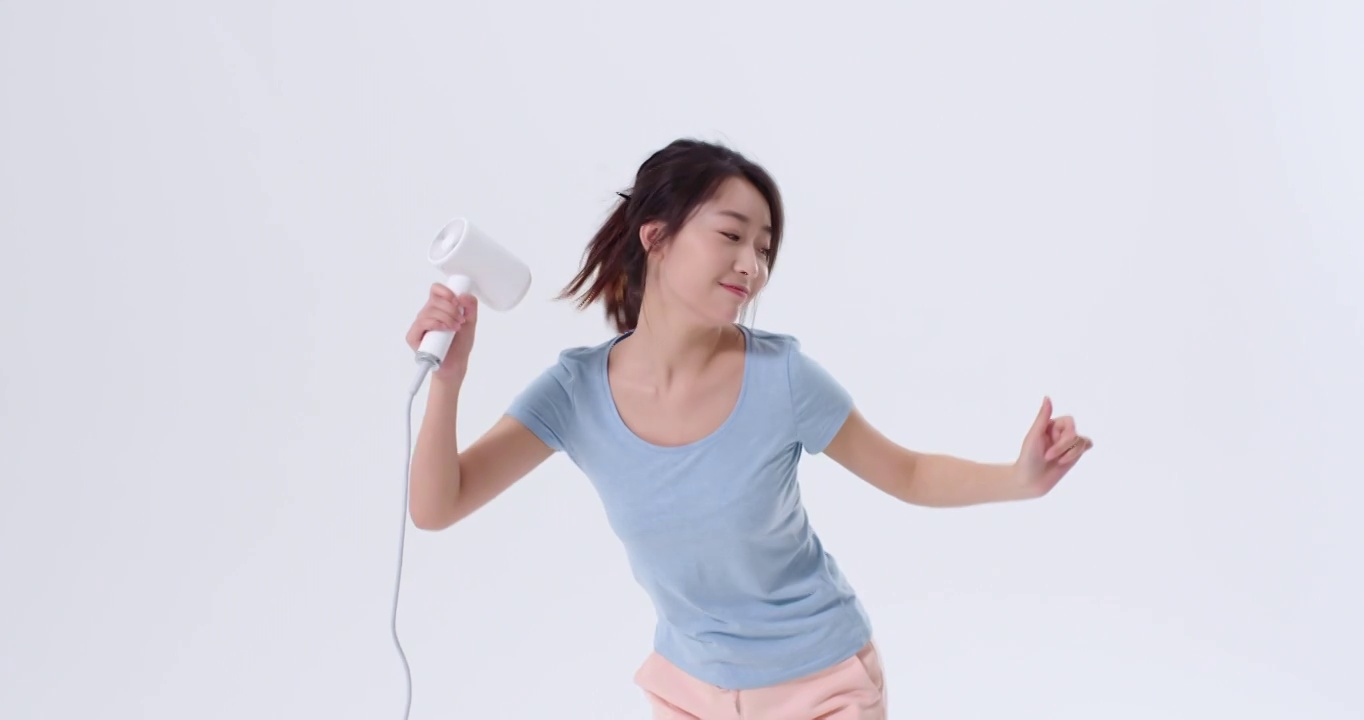 快乐的年轻女子拿着吹风机跳舞视频下载