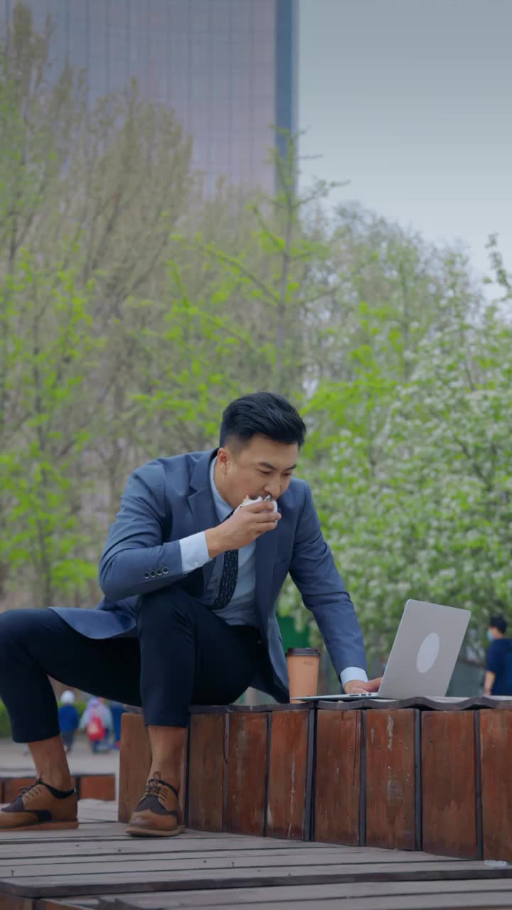 忙碌的商务男士在户外边吃饭边用电脑视频下载