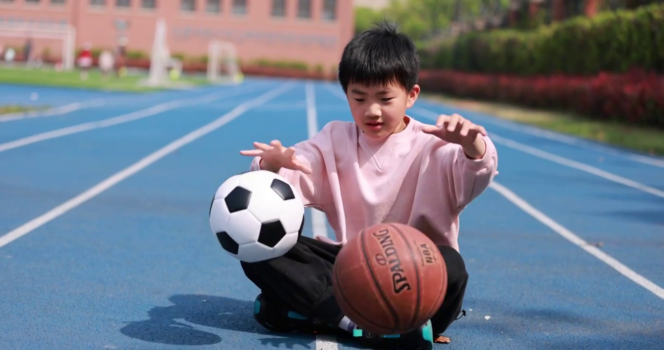 可爱的男孩坐在田径场玩球慢动作视频素材