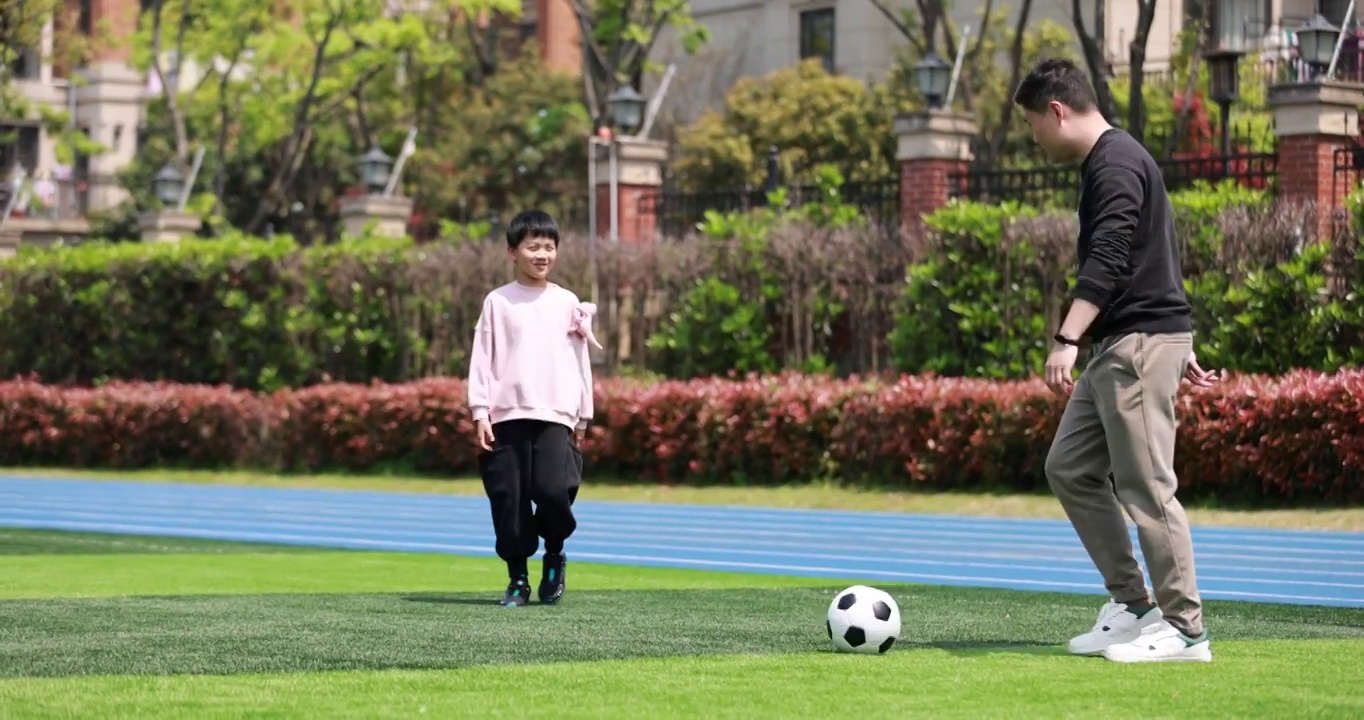 亚洲父亲和儿子在足球场上踢球视频素材