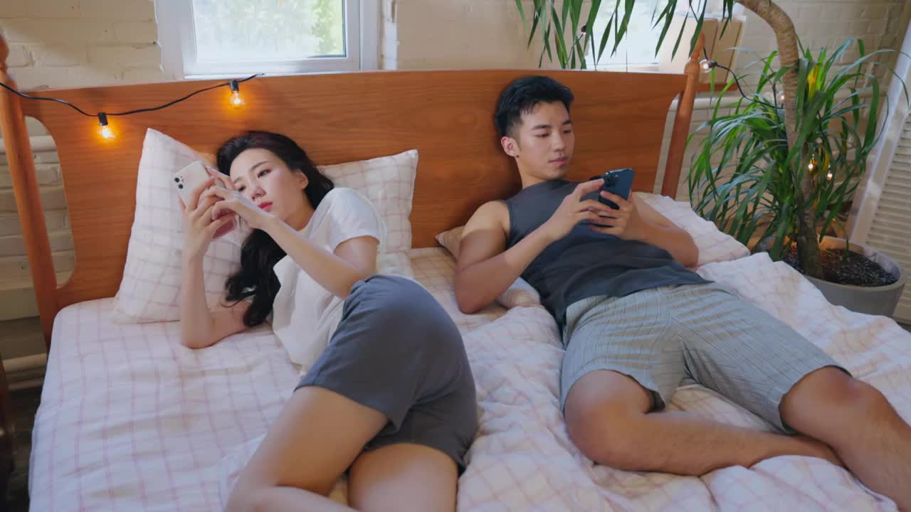 青年情侣躺在床上各自玩手机视频下载