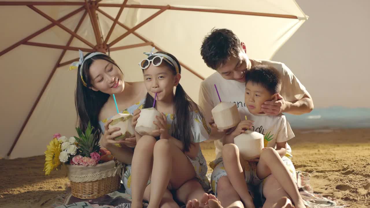 快乐的四口之家坐在沙滩上喝椰汁视频下载