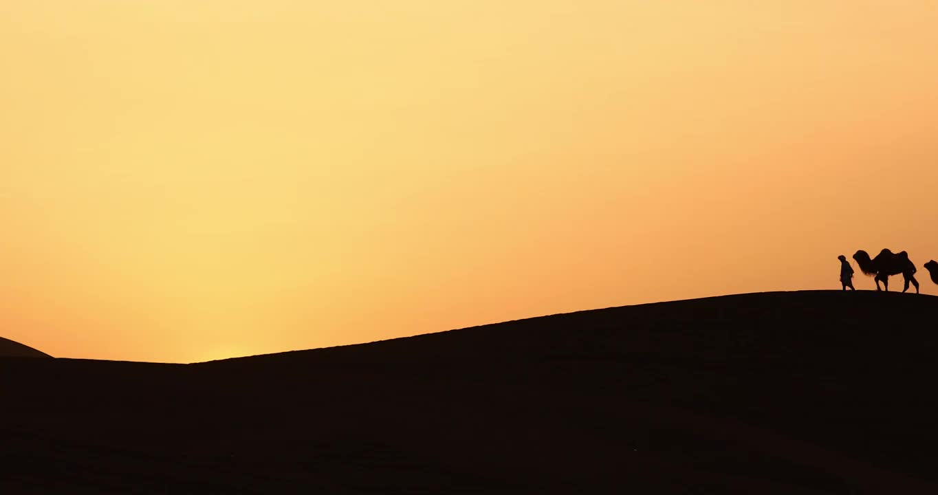 日落时沙漠的驼队，库木塔格沙漠的日落，塔克拉玛干沙漠的夕阳，夕阳下的骆驼与旅人视频下载