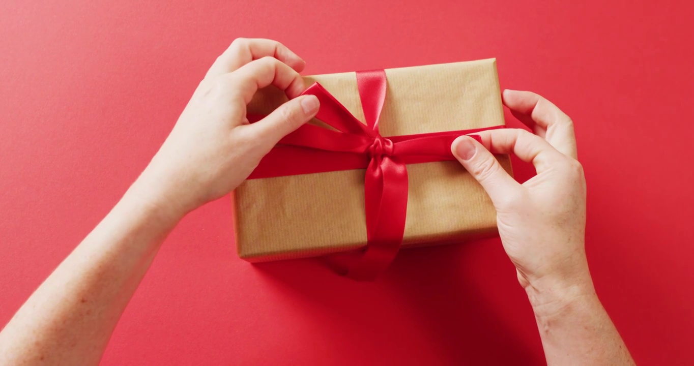 视频的手系红丝带礼盒包裹在牛皮纸，在红色背景视频下载