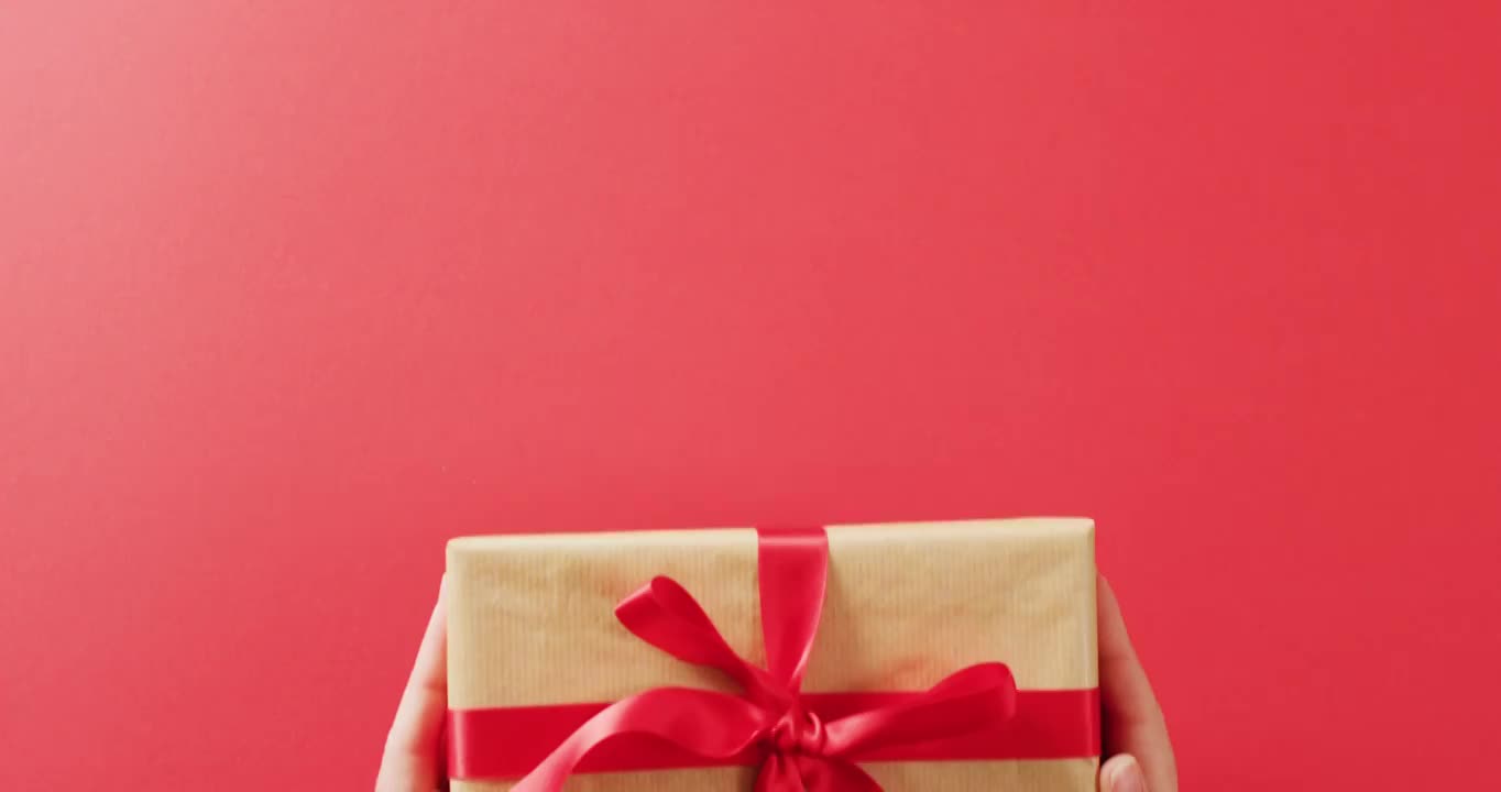 视频中的手把礼盒包裹在牛皮纸和红丝带在红色背景视频下载