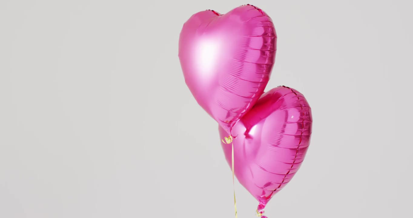 两个闪亮的粉色心形气球漂浮在白色背景上的视频，带有复制空间视频下载