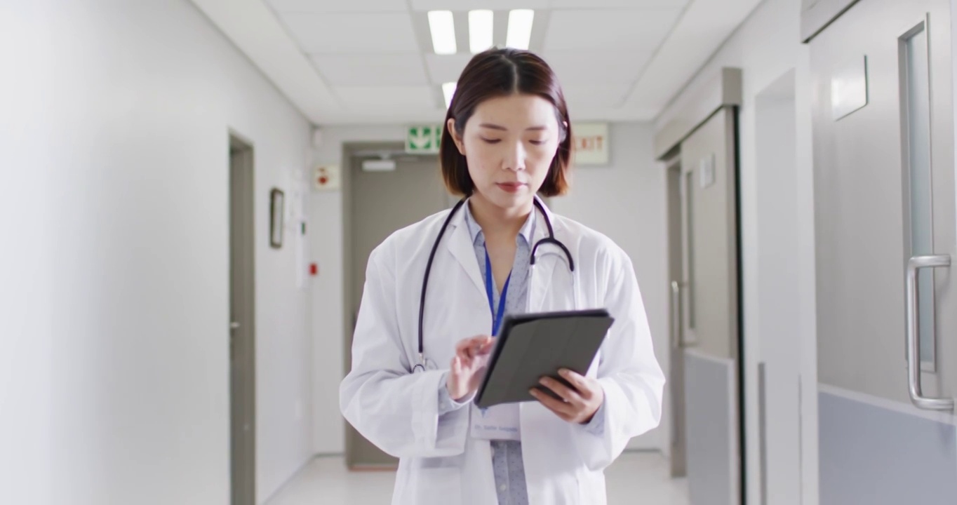 亚洲女医生走在医院走廊的视频，看着平板电脑，复制空间视频下载