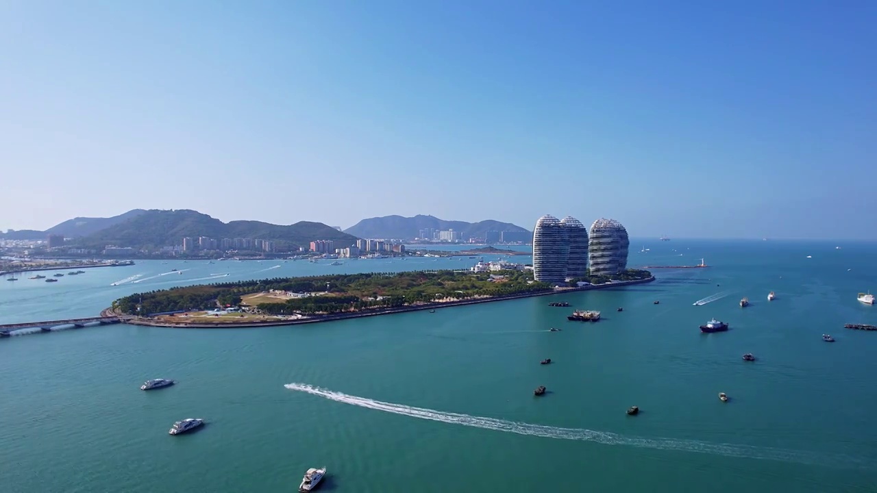 中国海南三亚三亚湾穿梭的游艇凤凰岛和城市天际线风光航拍视频素材