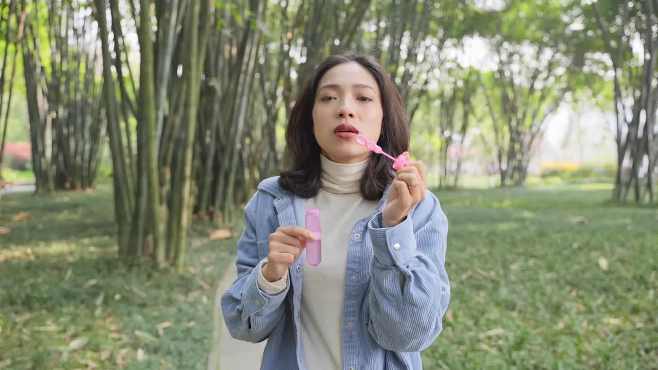 美女阳光竹林公园里对镜头吹泡泡特写视频下载