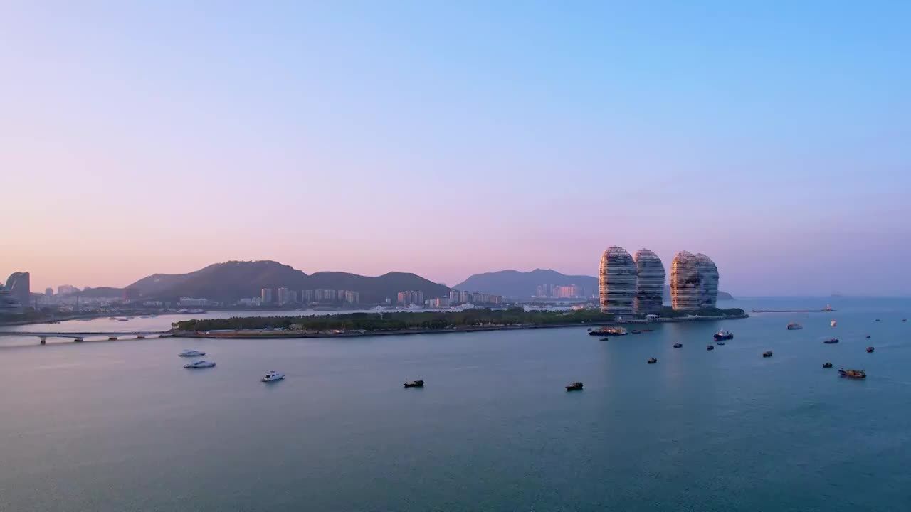 中国海南三亚三亚湾穿梭的游艇凤凰岛和城市天际线黄昏风光航拍视频素材