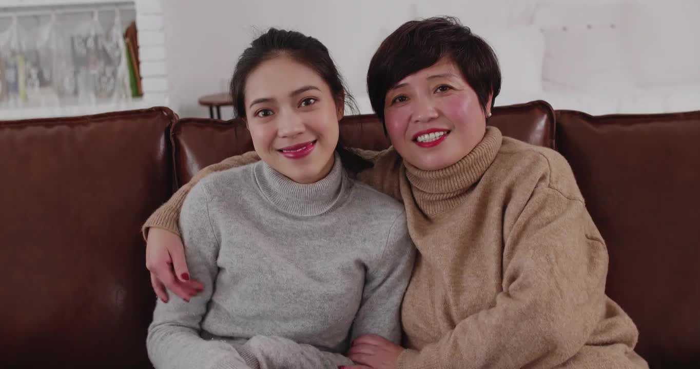 女儿和母亲微笑坐在沙发上看镜头视频聊天视频素材