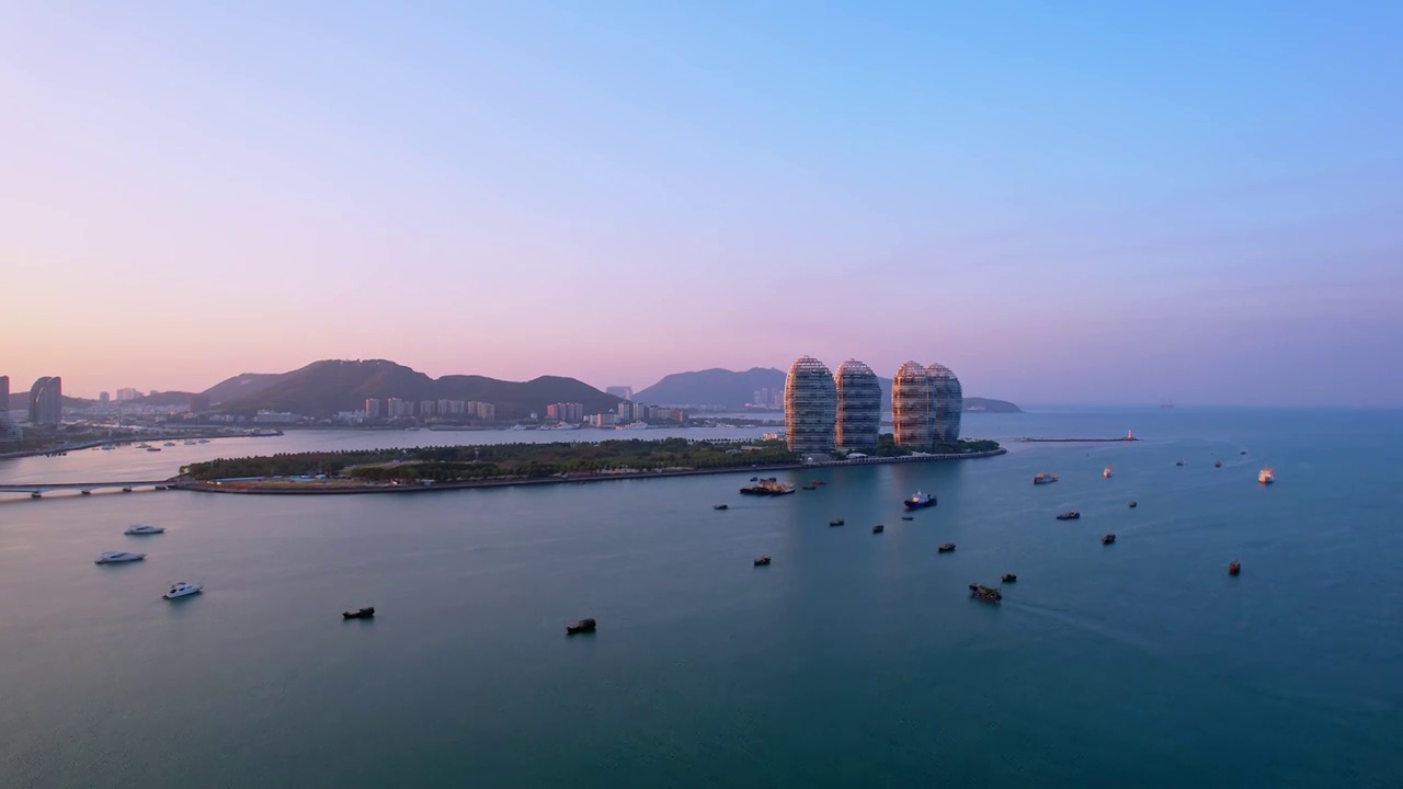 中国海南三亚三亚湾穿梭的游艇凤凰岛和城市天际线黄昏风光航拍视频素材