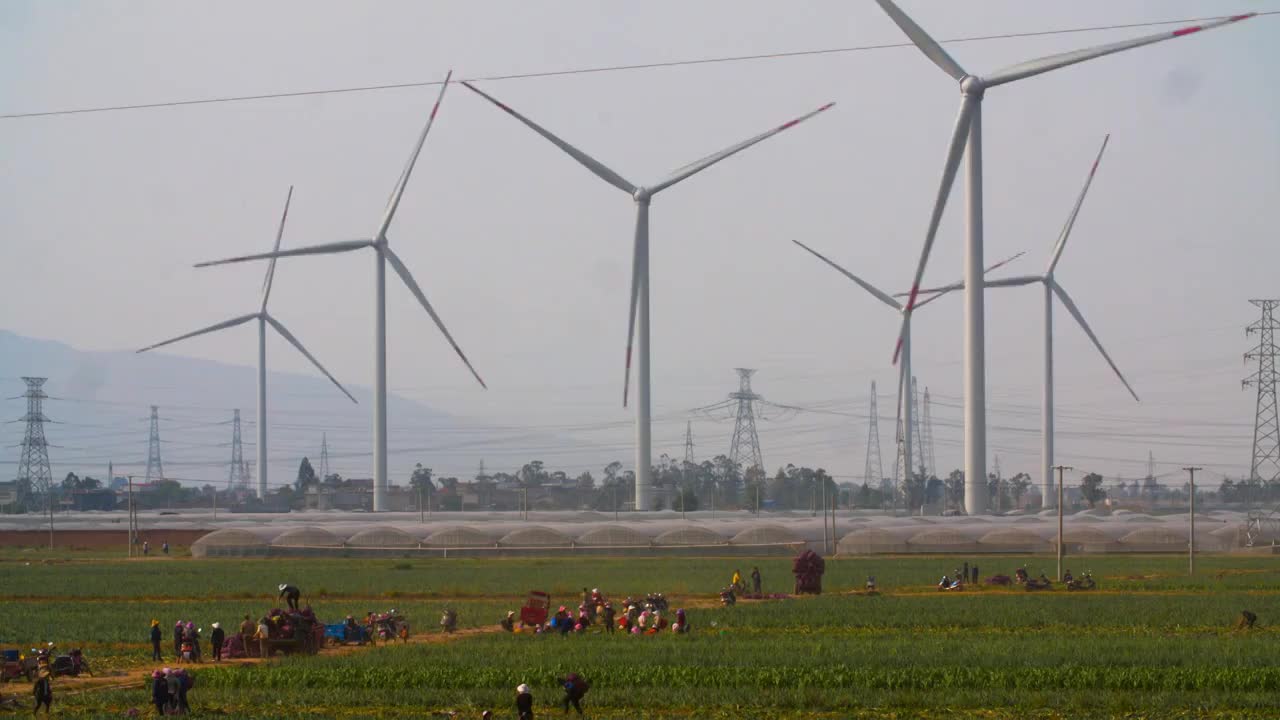风力发电机在大风中旋转农民在风中田地忙碌视频下载