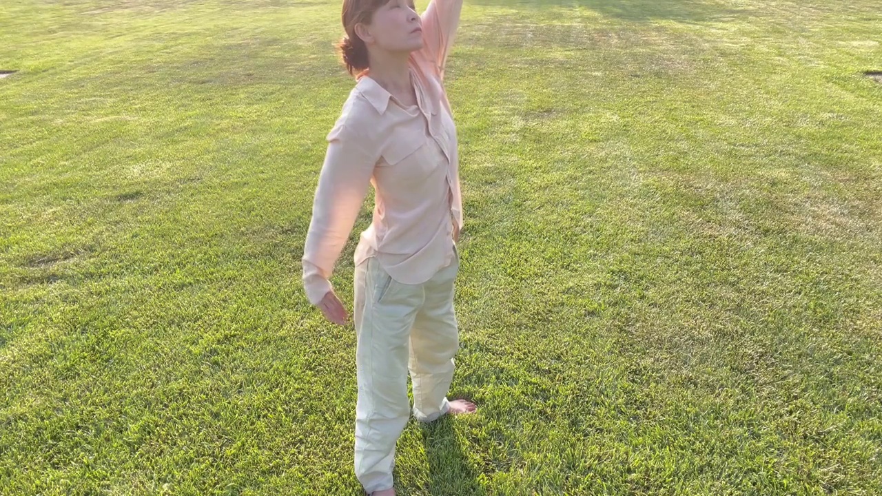 一个亚洲女人在草地上做健身气功八段锦视频下载