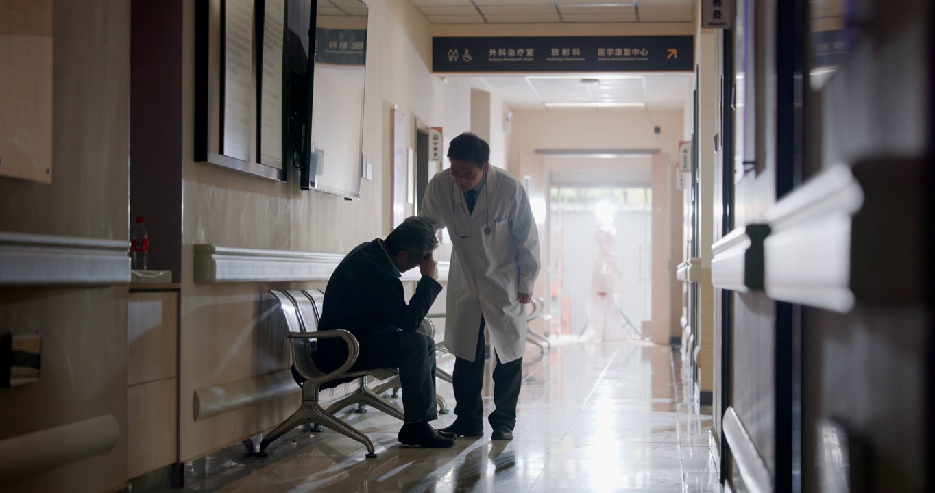 中年男医生安抚坐在医院走廊的老人视频下载