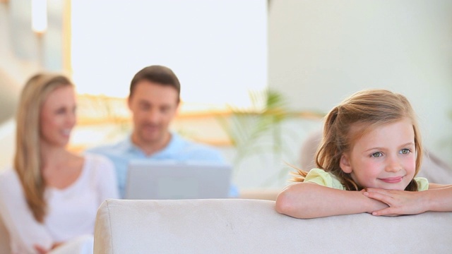 快乐的小女孩和她的父母在沙发上使用笔记本电脑的背景视频素材