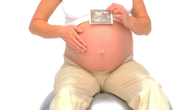 一名怀孕女性在健身球上拿着她未来宝宝的扫描图视频下载