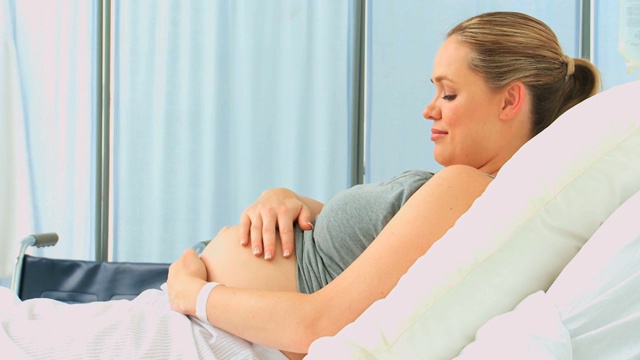 一名孕妇在诊所的床上摸着自己的肚子视频下载