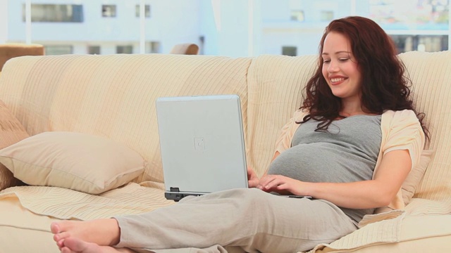 一名孕妇正在客厅里用笔记本电脑聊天视频下载