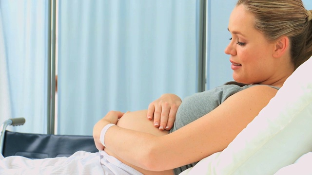 一名孕妇在诊所的床上抚摸着自己的肚子视频下载