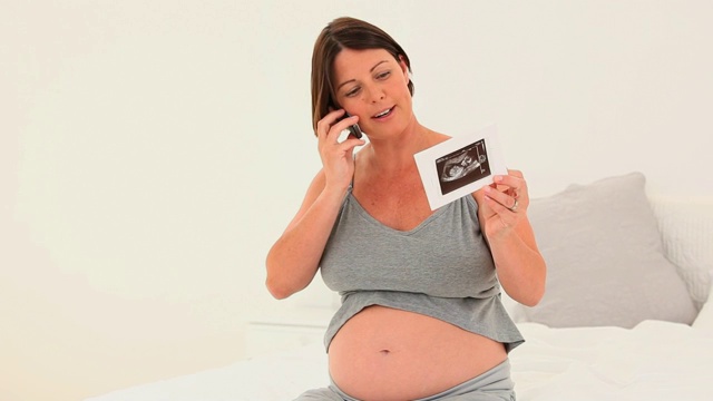 一名孕妇在客厅里打电话谈论她未来孩子的扫描图视频下载