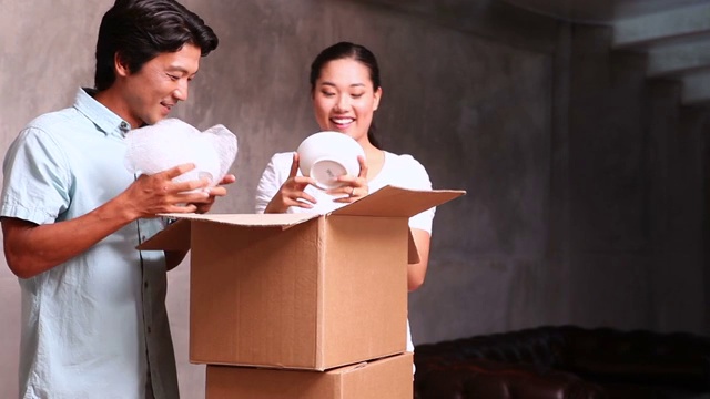 年轻的亚洲夫妇在他们的新家打开移动箱子视频素材