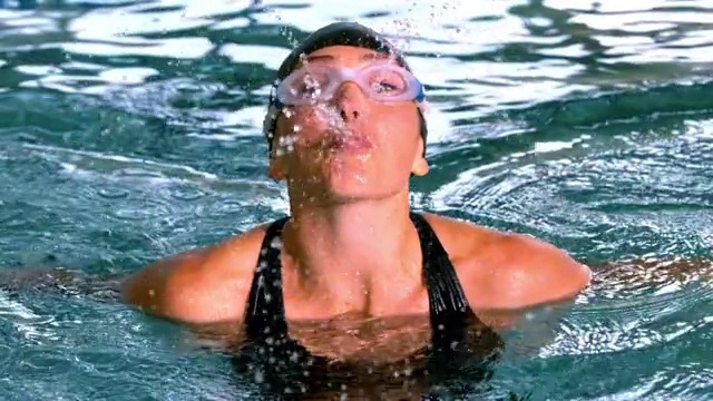有趣的女性游泳运动员在游泳池向镜头喷水的慢镜头视频素材