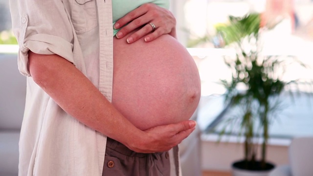 一名孕妇在起居室里摸着自己的肚子视频素材
