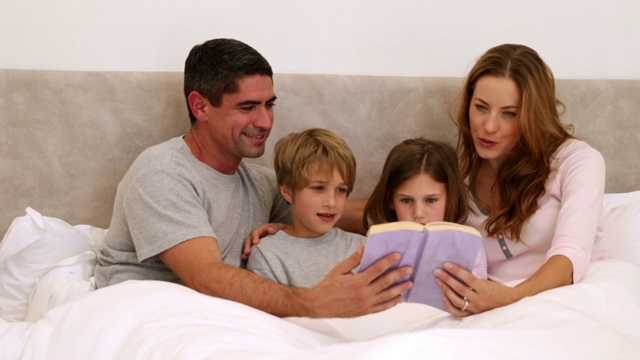 幸福的父母和孩子一起在卧室的床上看书视频下载