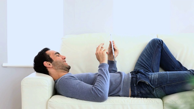 躺在沙发上的男人在用平板电脑视频素材