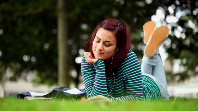 漂亮的学生躺在草地上听着音乐在大学读书视频素材